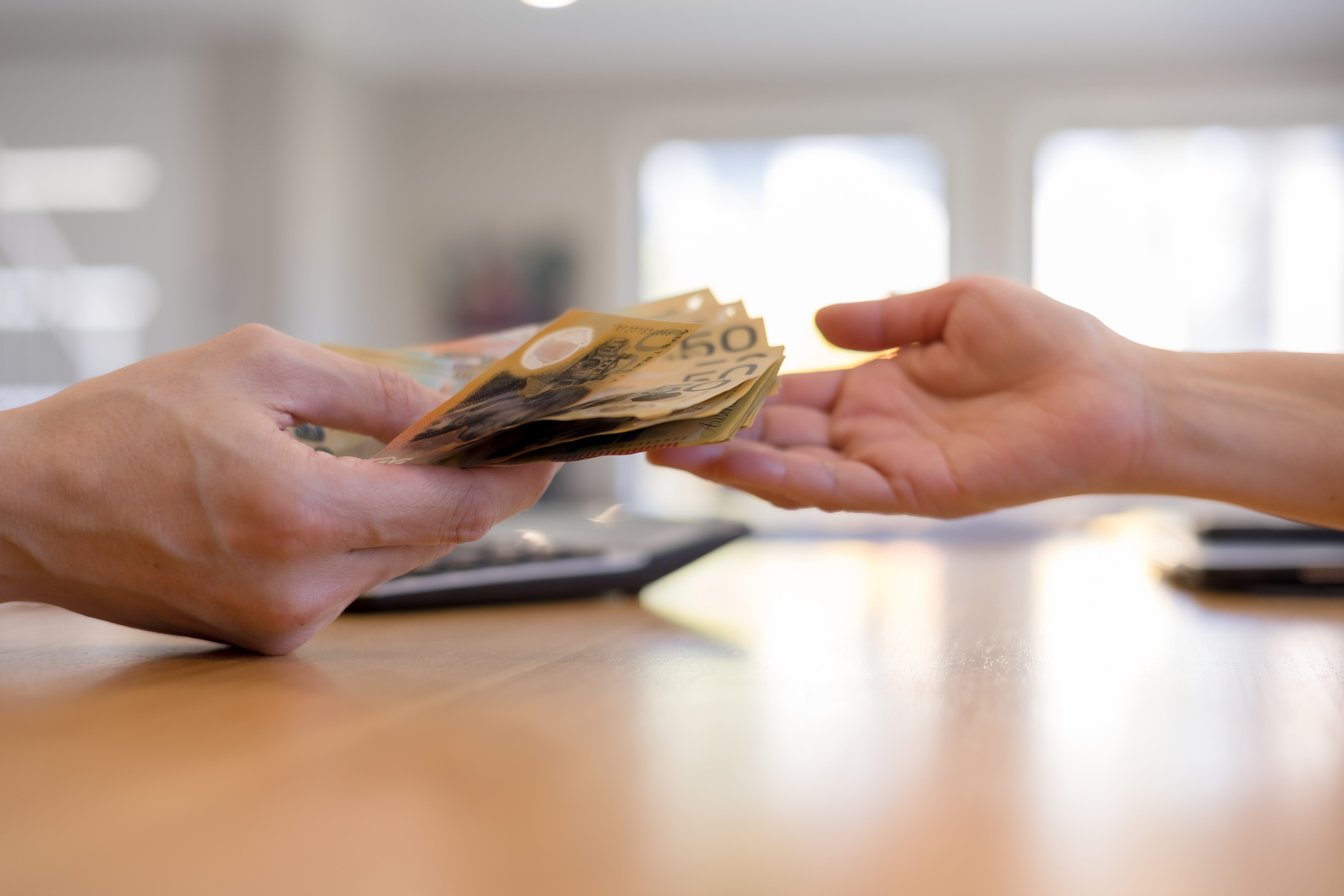 Close-up of hands exchanging Australian dollar banknotes across desk. Concept of cash payment, money transaction, financial exchange, business deal personal finance in everyday context.